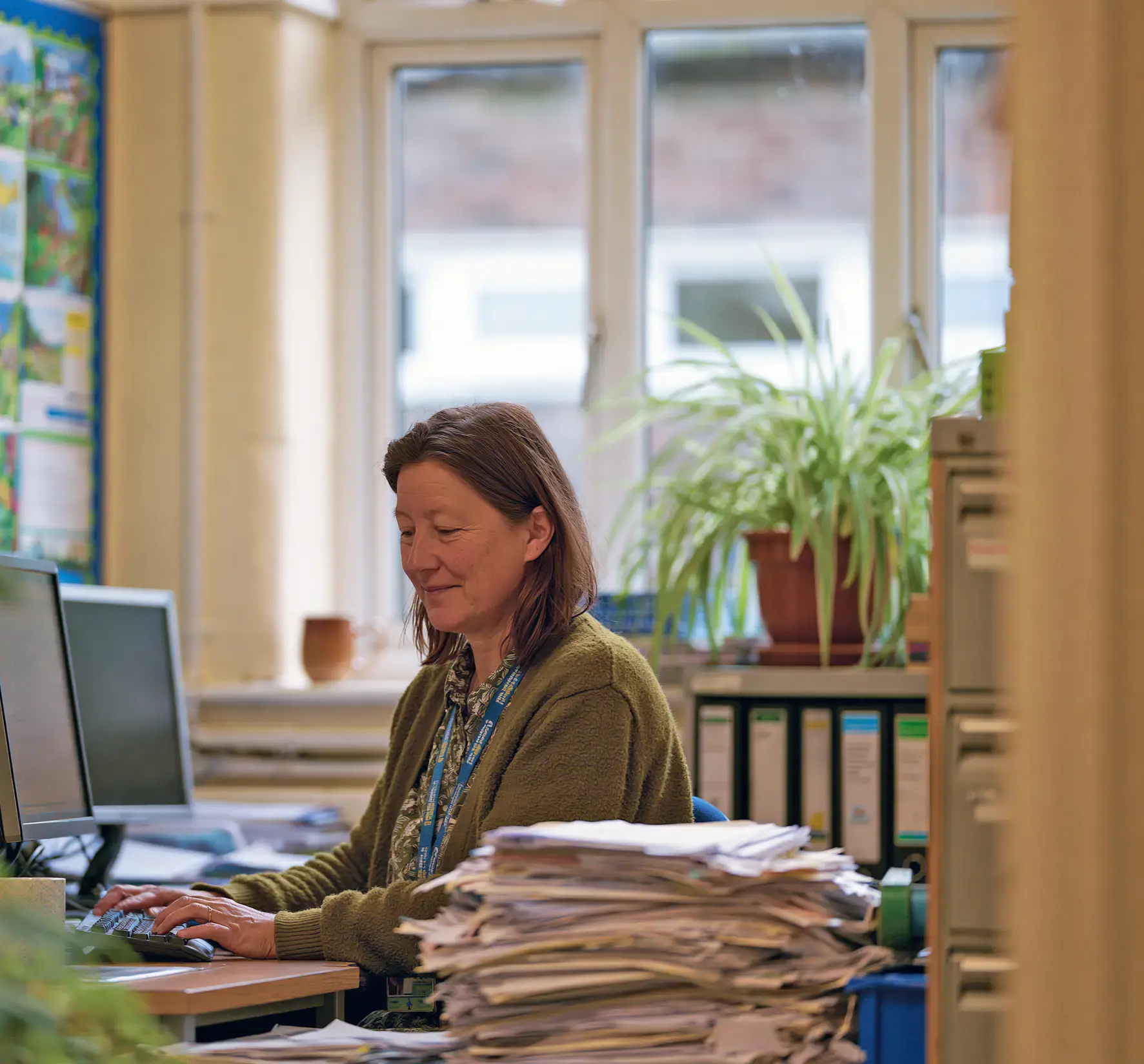 A teacher working at a computer with paperwork to one side
